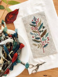 a white plate topped with scissors next to a piece of cloth and some thread on top of a wooden table