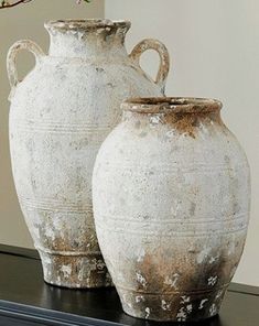 two white vases sitting on top of a black table next to each other with flowers in them