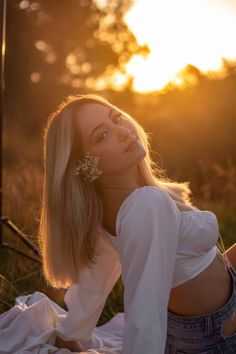 a woman sitting on top of a grass covered field next to the sun wearing earrings