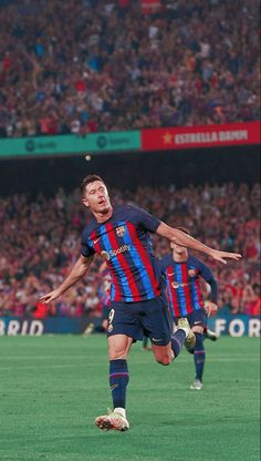 two men are playing soccer in front of an audience at a sporting event, one is about to kick the ball