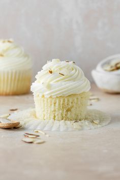 two cupcakes with white frosting and sprinkles on the table