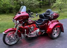 a red motorcycle parked on top of a parking lot next to grass and trees in the background