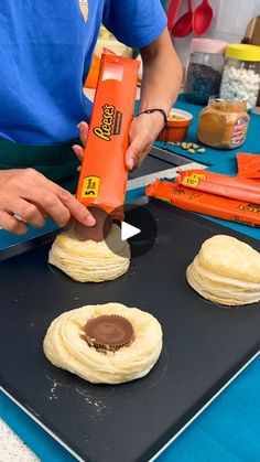 a person is using an orange machine to make pastries on a black tray with blue table cloth