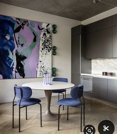 a white table with blue chairs in front of a large abstract painting on the wall