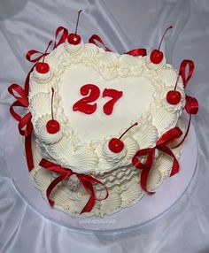 a heart shaped cake with red ribbons and cherries on it, sitting on a white table cloth