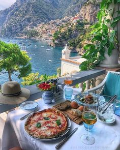 a table with pizza and drinks on it overlooking the water's edge in italy