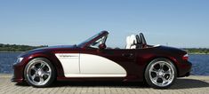 a red and white sports car parked next to a body of water