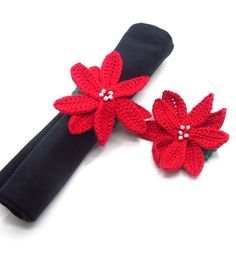 two red crocheted flowers with pearls on black fabric napkins next to each other