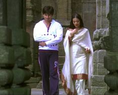 a man and woman standing next to each other in front of some stone pillars with columns