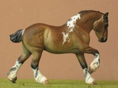 a brown and white horse walking across a green grass covered field in front of a tan wall