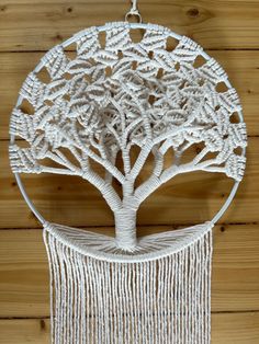 a white macrame hanging on a wooden wall with a tree in the middle