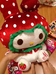 someone holding a hello kitty stuffed animal in front of a strawberry hat and candy bar