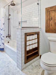 a white toilet sitting next to a bath tub in a bathroom under a wooden cabinet