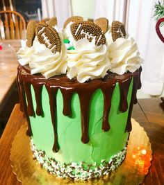 a green cake with white frosting, cookies and chocolate drizzle on top