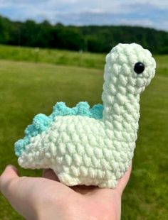 a hand holding a small crocheted llama in the middle of a field