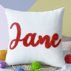 a white pillow with the word jane on it next to balls of yarn and crochet hooks