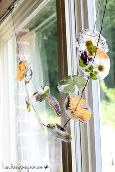 a wind chime hanging from the side of a window with flowers and leaves on it