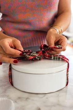 a woman tying a bow on top of a white box