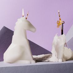 two white candles sitting next to each other in front of a purple and gray background