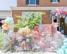 an assortment of balloons and decorations in front of a brick house with palm trees on the lawn