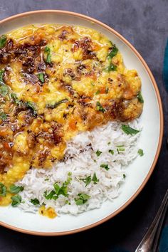 a white plate topped with rice and meat covered in sauce next to a fork on top of a blue table cloth