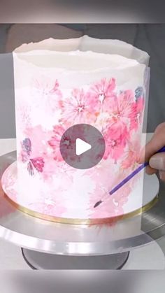 a person is painting a cake with pink flowers