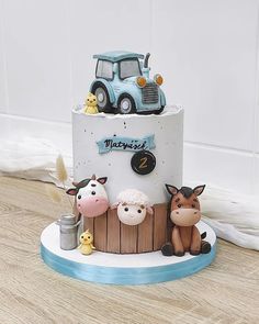 a birthday cake with farm animals on top and a tractor in the background, sitting on a wooden table