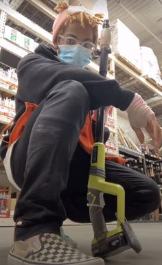 a person with a face mask sitting on a shopping cart in a store holding a tool