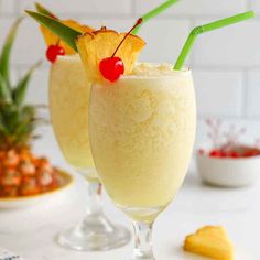 two glasses filled with pineapple milkshakes and topped with cherries