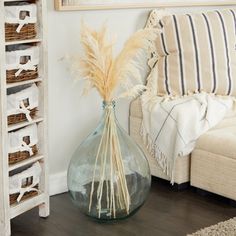 a vase filled with dry grass sitting on top of a wooden floor next to a couch