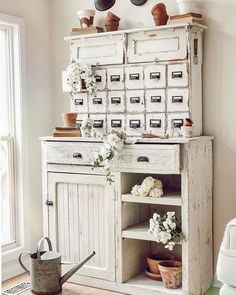 an old white cabinet with flowers and pots on top is in the corner of a room