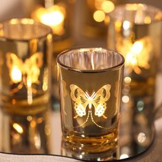 three glasses with butterfly designs on them sitting on a table next to candles and napkins