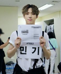 a young man holding up a sign with the words ateez on it in front of his face