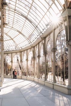 two people are standing in the middle of a large room with glass walls and arched windows