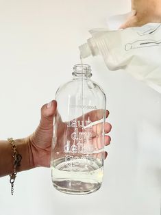 a person holding a glass bottle with water in it and another hand reaching out to the bottle