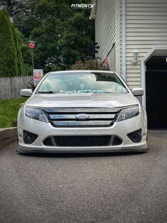 the front end of a silver car parked in front of a garage with its door open