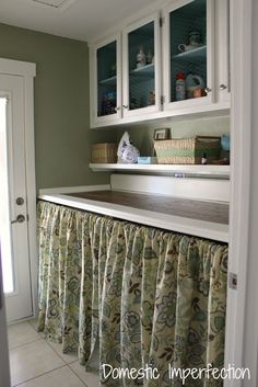 a kitchen with white cabinets and curtains on the window sill, along with a curtained counter