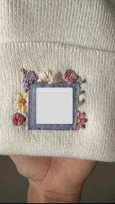 a hand holding a white hat with flowers on the side and a small photo frame attached to it