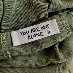 a label that says you are not alone on the back of a green shirt with white lettering