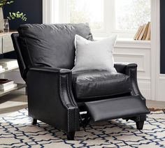 a black leather chair with two white pillows on it in front of a blue and white rug