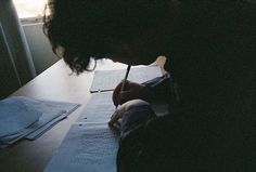 a person sitting at a table writing with a pen and paper on top of it