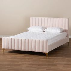 a pink bed with white sheets and pillows on top of wooden flooring next to a beige wall