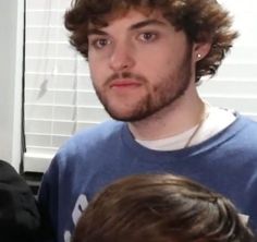 a man in a blue shirt is standing next to another man with curly hair and an earring