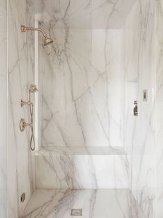 a bathroom with white marble walls and flooring, including a walk in shower area