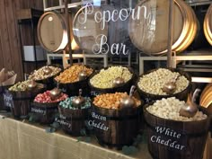 several wooden buckets filled with different types of popcorn on a table next to barrels