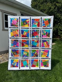 a multicolored quilt on the grass in front of a house