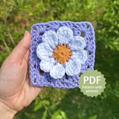 a crocheted square with a flower on it in the palm of someone's hand