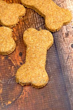 four dog biscuits on a wooden table with one bone shaped like a human's head