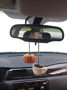 a car dashboard with a coffee cup hanging from the dash board and a knitted pumpkin hanging from the rearview mirror