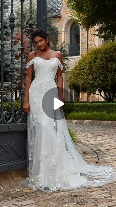 a woman standing in front of a gate wearing an off the shoulder white wedding dress